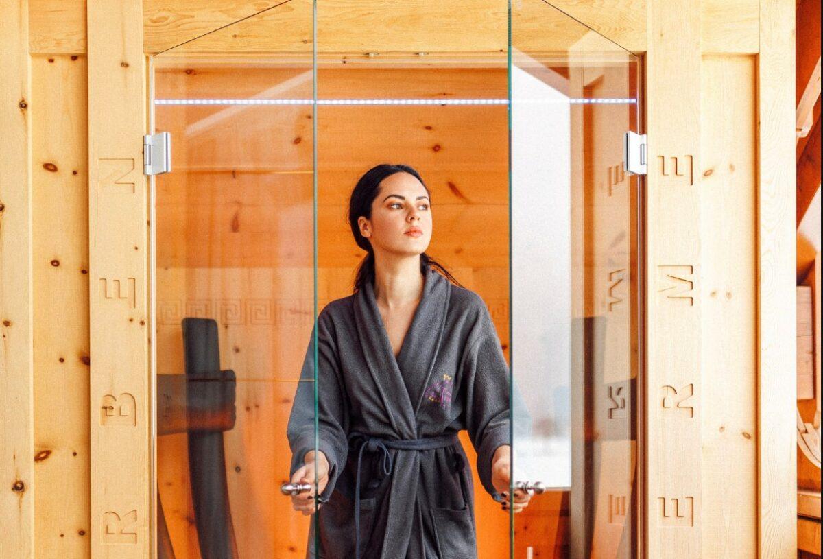 A woman wearing a bathrobe emerges from the sauna. The sauna is powered by sustainable solar energy.