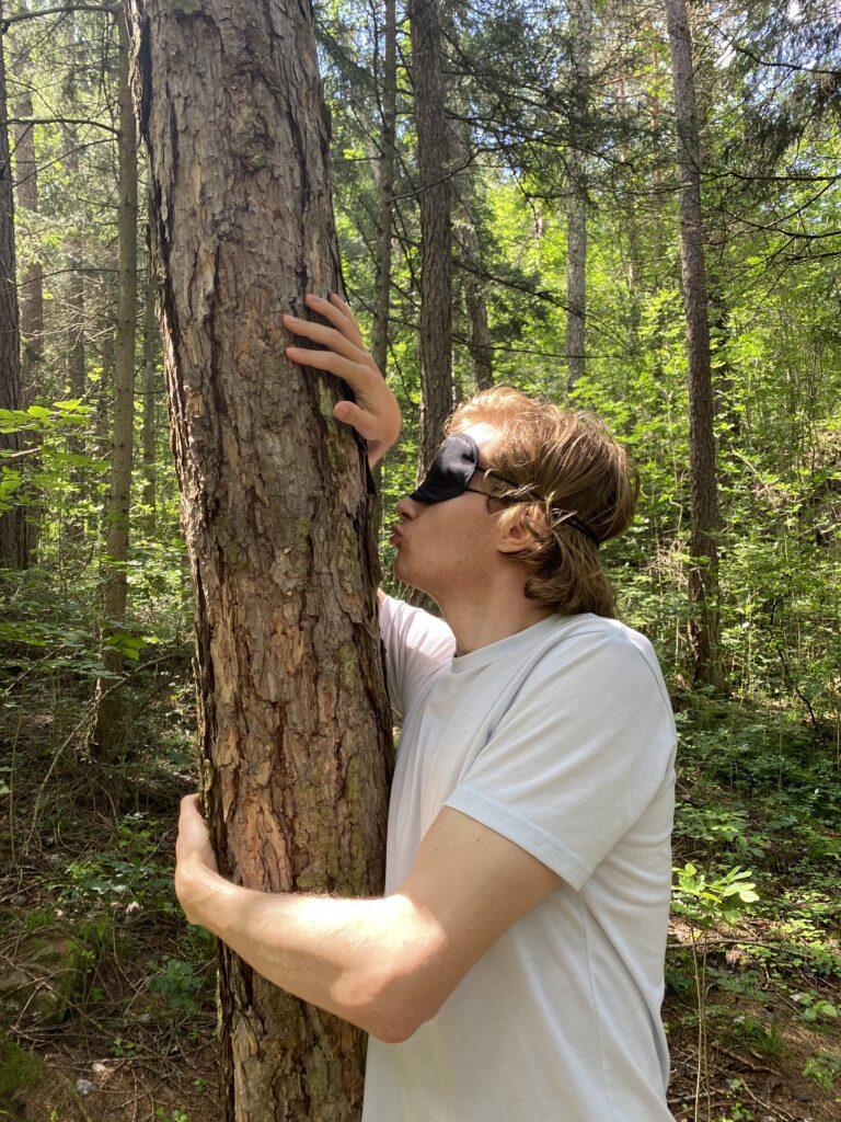 A man wearing an eye mask kisses a tree while forest bathing in Naturns, South Tyrol